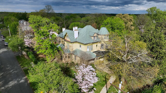 Aerial view of a historic house with a green roof surrounded by lush spring trees and a blooming dogwood in a residential neighborhood in Lynchburg, Virginia, United States.