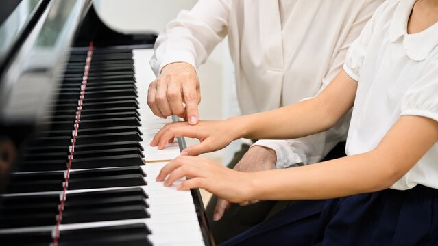 Close-up of a piano teacher guiding a child's hands on piano keys during a lesson