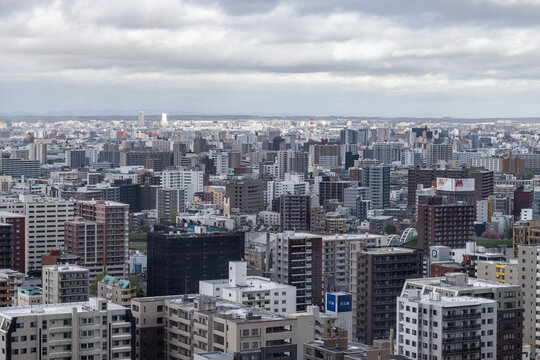 Aerial view of the dense urban cityscape of Sapporo, featuring residential and commercial buildings, high-rise apartments, and a sprawling metropolitan landscape in Sapporo, Hokkaido, Japan.