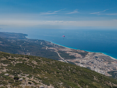 Aerial view of a paraglider soaring over the Llogara Pass with the Ionian Sea coastline, winding roads, and mountainous terrain in Llogara, Vlore County, Albania.