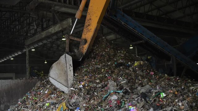 Heavy machinery dumps huge piles of mixed trash in an industrial recycling center. A stark look at waste management, pollution, and the need for global sustainability.