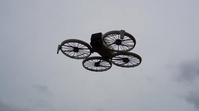 A modern drone with four large spoked wheels hovers against an overcast sky, showcasing its unique design and flight capability in a minimalist aerial shot, highlighting flight drone elements.