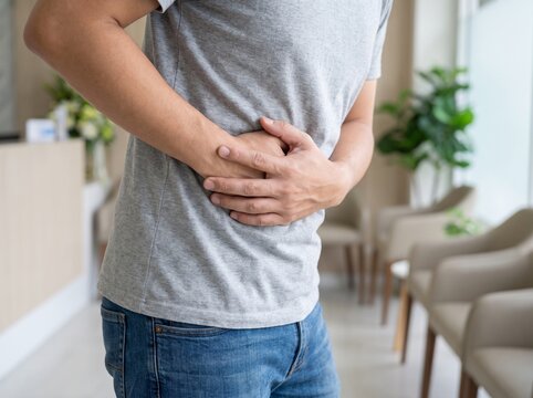 Man standing in a clinic waiting room holding his abdomen experiencing stomach ache, side pain, or digestive issues.