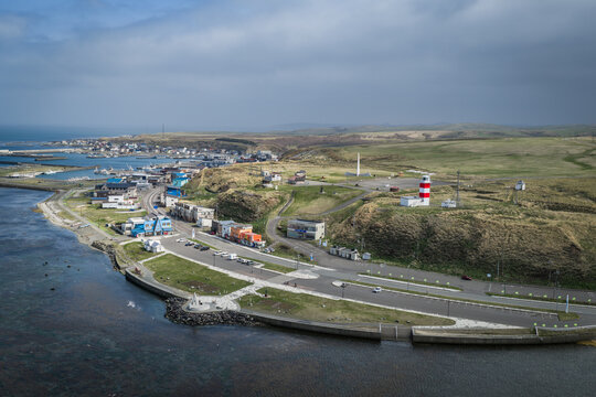 Aerial view of Cape Soya with its iconic red and white lighthouse, coastal road, and surrounding grassy hills overlooking the sea in Wakkanai, Hokkaido, Japan.