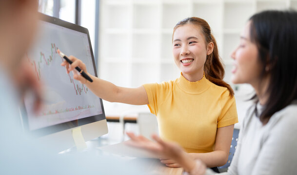 Asian Businesswoman Smiling and Pointing Pen at Computer Monitor