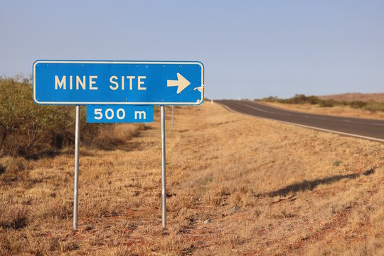 Blue road sign in outback pointing toward mine site five hundred meters ahead. Empty country highway under clear sky. Regional Australia. Copy space for text