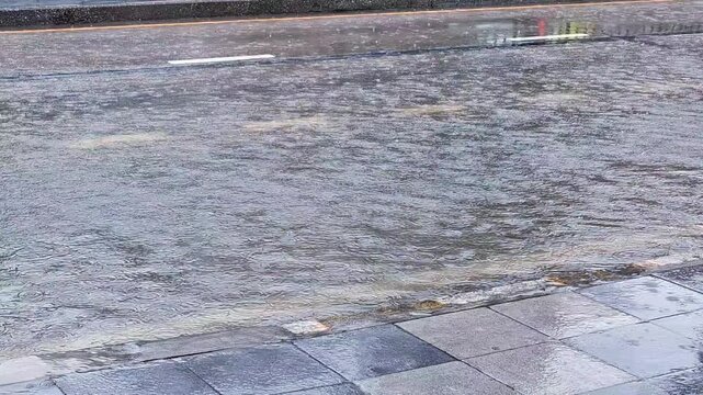 Rainwater flowing rapidly across flooded asphalt street and sidewalk pavement