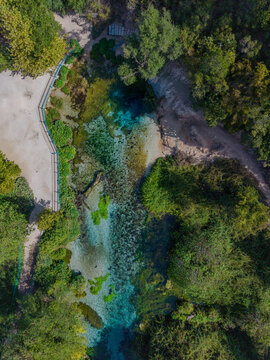 Aerial view of The Blue Eye, a natural spring with vibrant turquoise water surrounded by lush green forest and walking paths in Saranda, Qarku i Vlores, Albania.