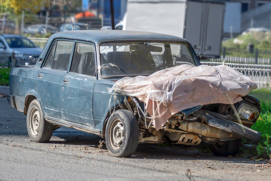 An old wrecked car is parked on the street on an autumn day