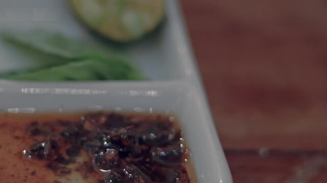 Close-up detail shot to a piece of vietnamese fried springrolls (Cha Gio) being dipped in chili oil (sa te), candid authentic foodie experience