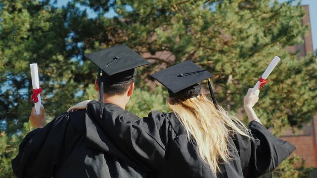 Happy graduates standing together outdoors holding diploma scrolls in hands during sunny day.