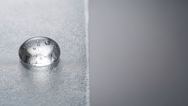 A single large water drop with internal air bubbles on a textured grey surface with space for text