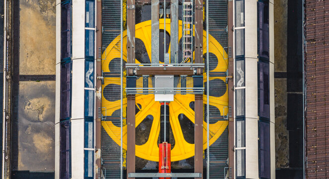 Aerial view of a massive yellow drive wheel and mechanical system powering a mountain cable car in the Italian Dolomites, Selva, Trentino-Alto Adige, Italy.