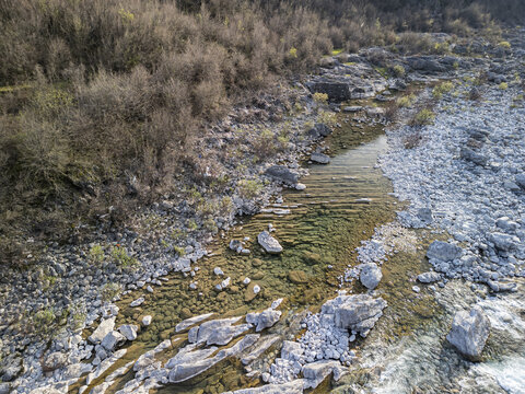 Aerial view of the Kiri River with clear water flowing over a rocky riverbed, stones, pebbles, sparse vegetation, and dry bushes, Shkoder, Qarku i Shkodres, Albania.
