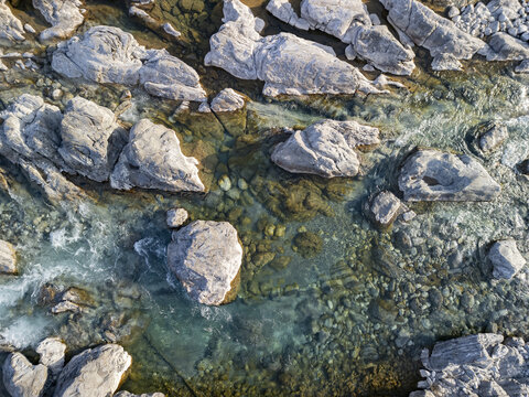 Aerial view of Lume i Kirit with clear turquoise water flowing over smooth grey river stones and boulders in Shkoder, Qarku i Shkodres, Albania.