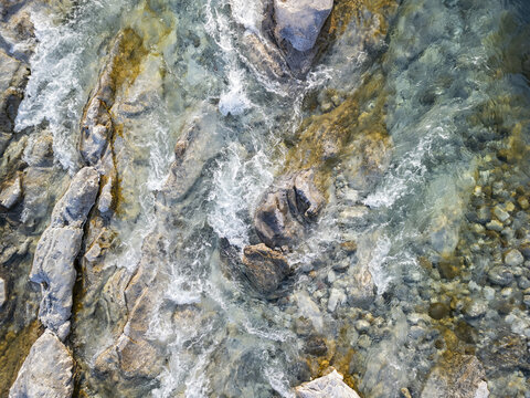 Aerial view of the clear flowing waters of the Lume i Kirit river, featuring rocky riverbed, smooth stones, and turbulent currents in Shkoder, Qarku i Shkodres, Albania.