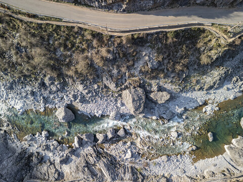 Aerial view of the rocky bed of the Kiri River with turquoise water flowing through rugged terrain and a winding road nearby in Shkoder, Qarku i Shkodres, Albania.