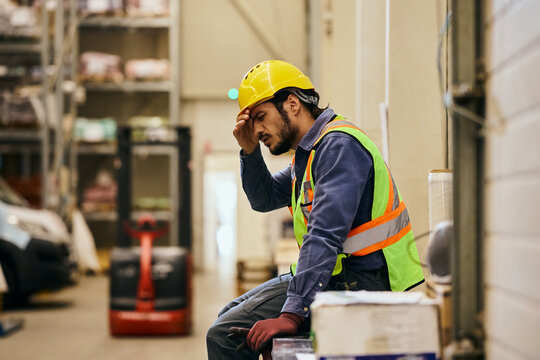Tired worker with headache resting during shift in distribution warehouse.