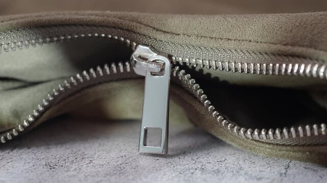 Macro view of silver metal zipper moving slowly on olive green suede fabric background