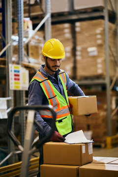 Warehouse worker analyzing inventory list while working with packages in storage room.