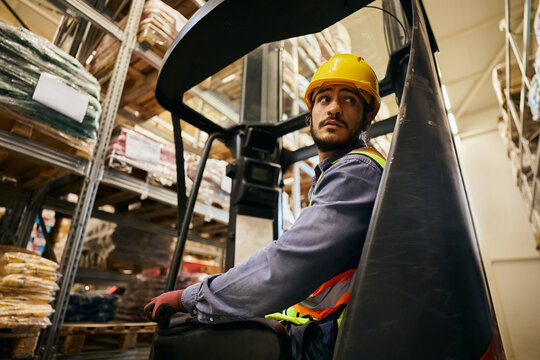 Warehouse worker driving forklift in storage compartment.