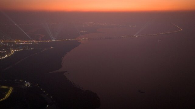 Aerial view of the illuminated bridge stretching across the water at dusk with city lights glowing in the distance, Nagda, Madhya Pradesh, India.
