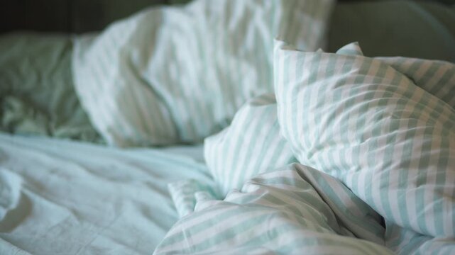 Close up of an unmade bed with crumpled sheets and pillows, showcasing a cozy and relaxed morning atmosphere with soft focus movement
