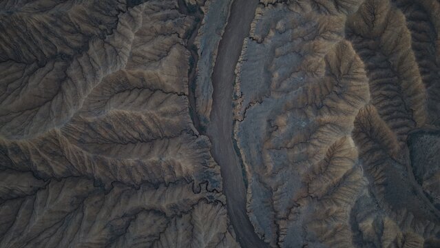Aerial view of the rugged, eroded landscape near Issyk Kul, featuring deep canyons, intricate ridges, and dramatic shadows cast across the arid terrain in Issyk-Kul Region, Kyrgyzstan.