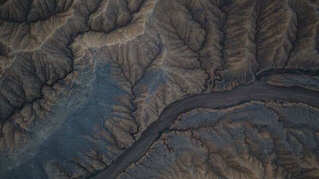 Aerial view of the rugged arid landscape with deep erosion patterns, ridges, and a dry riverbed winding through the terrain near Issyk Kul in Issyk-Kul Region, Kyrgyzstan.