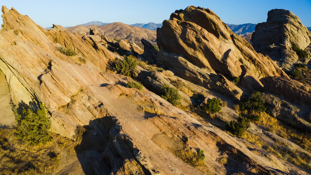 Aerial view of the iconic tilted sandstone rock formations of Vasquez Rocks with rugged terrain, desert vegetation, and clear blue sky in the United States.