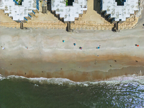 Aerial view of beachfront buildings with sandbag fortifications along the shoreline, with people on the sand and Atlantic Ocean waves in North Topsail Beach, North Carolina, United States.