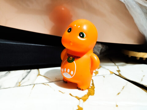 Orange dinosaur toy stands on marble surface