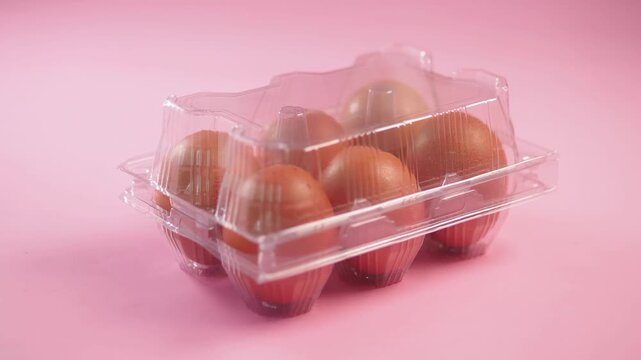 Close up view of fresh brown eggs in plastic box on pink background, eggs for breakfast, ingredient for baking, food preparation