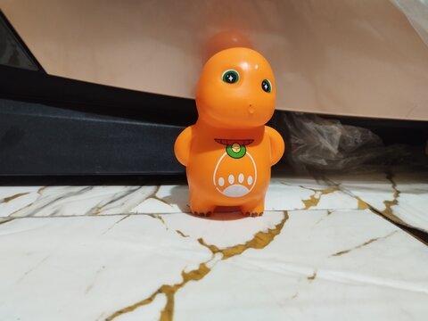 Orange dinosaur toy stands on marble surface