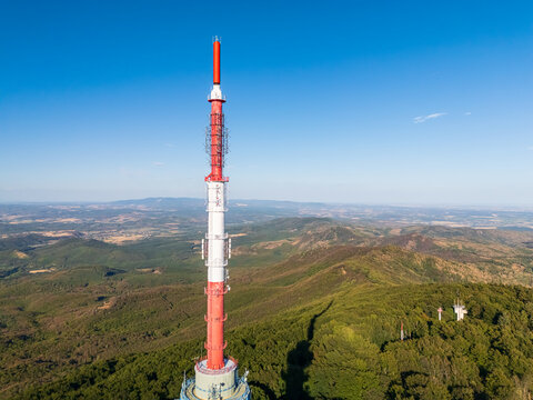 Aerial view of Kekes TV Tower and observation tower in the Matra Mountains, Hungary, above forested slopes under blue summer sky, with broadcasting and telecommunication infrastructure