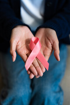 Close-up of a woman's hands gently holding a pink ribbon for breast cancer awareness campaign. Asian female patient support, healthcare, and hope concept. Vertical Shot