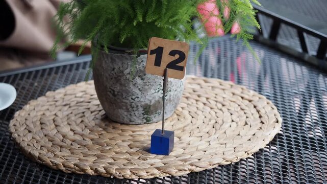 Outdoor cafe table with green plant pot and wooden number twelve sign on wicker mat