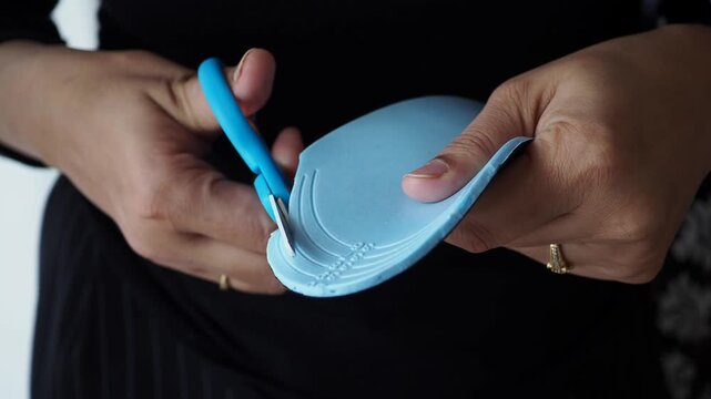 Woman hands cutting blue orthotic shoe insole with scissors to fit size