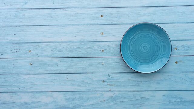 Top view of hand placing colorful ceramic plates on blue wooden table