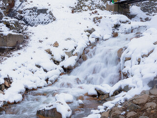 Mountain stream cascading through snowy banks © Abetehaael
