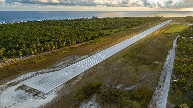 Aerial view of Tikehau Airport runway surrounded by dense palm forests and the Pacific Ocean in The Tuamotu and Gambier Islands, French Polynesia.