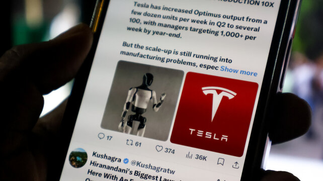 Smartphone displaying social media post about Tesla Optimus robot production updates.