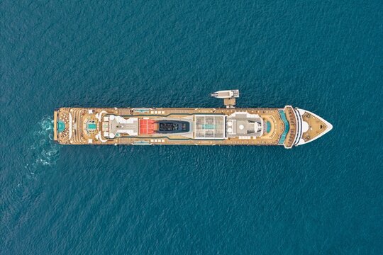 Aerial view of a large cruise ship sailing near the coast of Ile Sainte-Marguerite, showing the deck layout, swimming pools, and deep blue sea in Cannes, Provence-Alpes-Cote d'Azur, France.