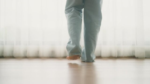 Close up view barefoot young Asian woman walking towards room window opens curtains