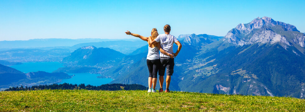 Happy couple hikers embracing on mountain top looking at lake and alps landscape view