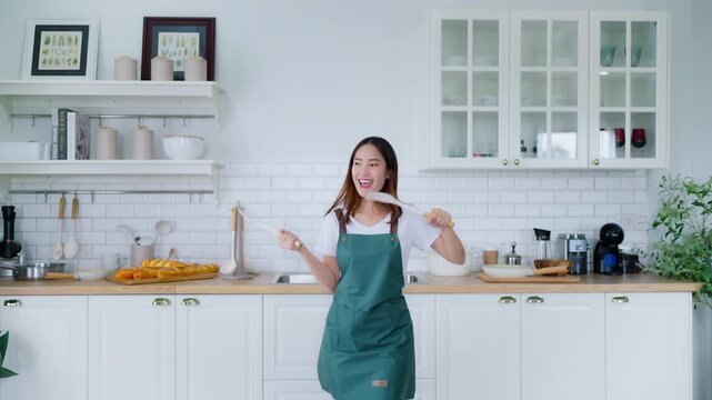 Young Asian woman dancing in the kitchen. The joy of a beautiful woman relaxing in her free time during the weekend in the house