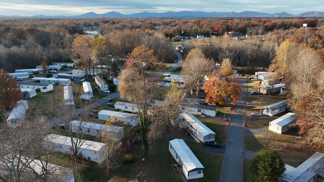 Aerial view of a mobile home park in Lynchburg during autumn, featuring rows of white trailers, fall foliage, and distant mountains, Lynchburg, Virginia, United States.