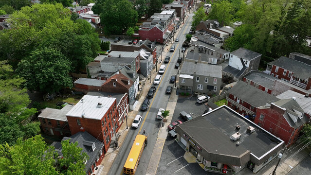 Aerial view of a yellow school bus driving down a street lined with historic brick buildings and lush green trees in South Lancaster, Lancaster, Pennsylvania, United States.