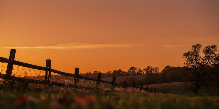 Orange sunset sky over rustic wooden fence silhouette on autumn countryside, warm glowing horizon at dusk, peaceful rural landscape background