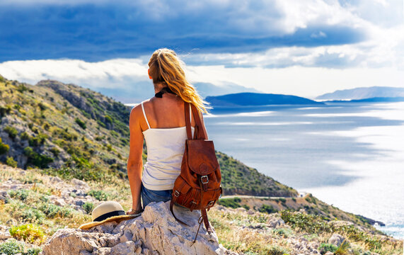 Young woman hiker sitting on mountain peak looking at dramatic sea view